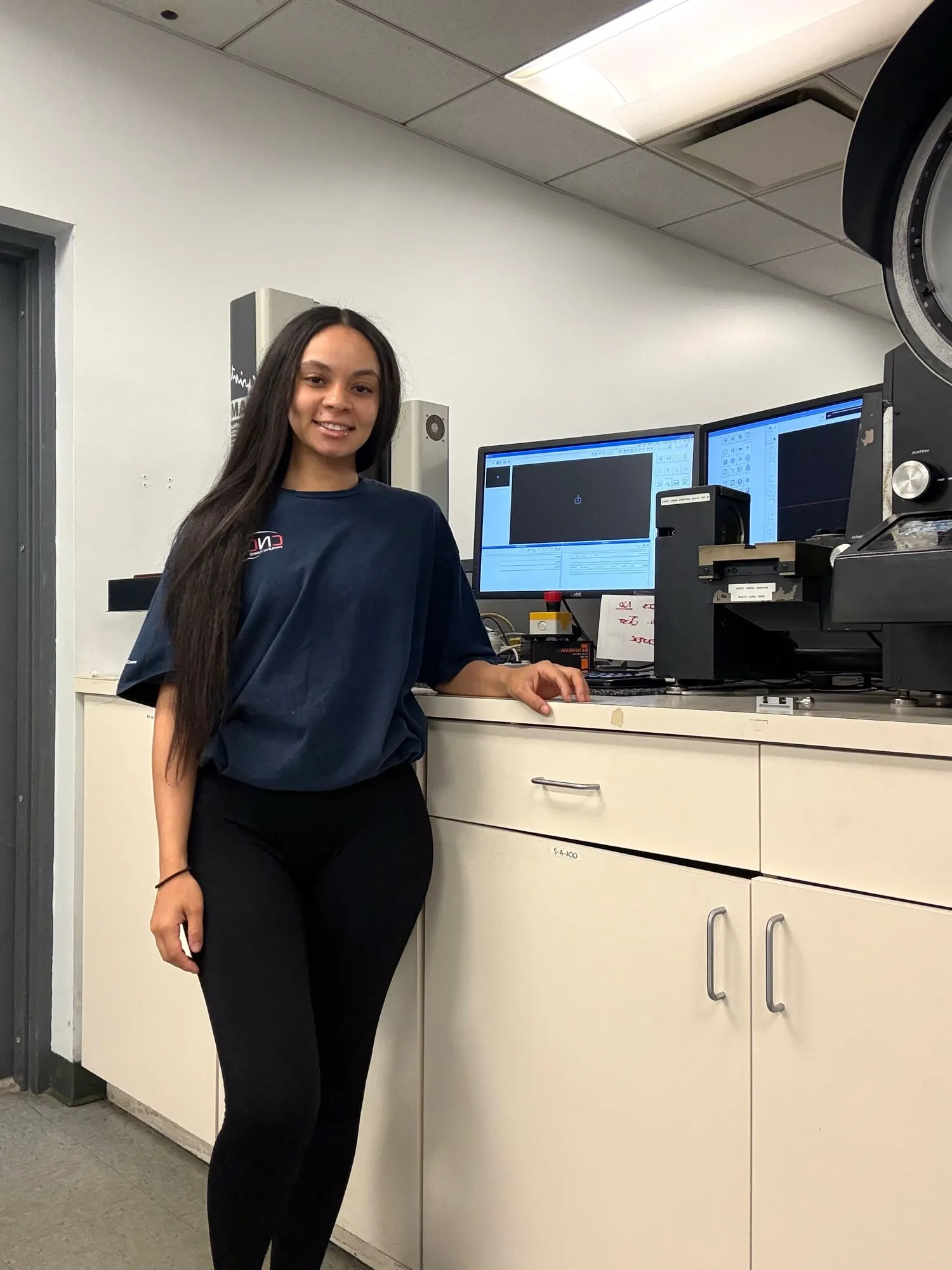 A CNC Manufacturing team member in the climate-controlled metrology lab, beside the optical measurement equipment