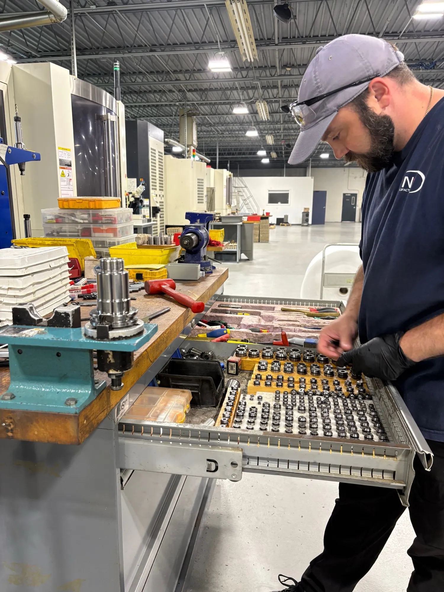 A machinist setting tooling at the tool-presetting bench, with collets and tool holders laid out